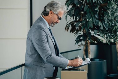 Havaalanındaki Olgun İşadamı Sigorta Analizi Belgeleri. Seyahat sigortası başvurusu: Ciddi bir işadamı elinde telefon, kahve ve seyahat sigortası poliçesiyle masada duruyor.