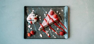 Bir kafede bir dilim ahududu keki, siyah tabakta. Sağlıklı ahududulu kek masası. Siyah tabakta meyveler ve fındıklar bir restoranda yemeye hazır..