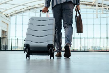 Havalimanı Terminal Salonunda Evrak Çantası ve Bavulla Yürüyen Gri Takım Elbiseli Tanınmayan İş Adamı Düşük Açı Görünümü