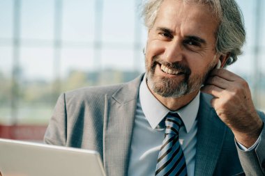 Olgun İşadamı Portresi Kablosuz Kulaklık takıyor ve Havalimanında Dijital Tablet Kullanıyor