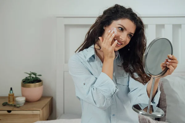 Happy Woman Holding Mirror Het Toepassen Van Gezichtscrème Haar Slaapkamer — Stockfoto