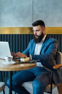 Ciddi bir iş adamı lüks bir restoranda espresso içip pasta yerken dizüstü bilgisayarında iş raporu yazıyor.