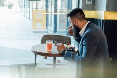 Restoranda kek yerken cep telefonu kullanan yakışıklı bir iş adamı. Evet. Aç işadamı bir kafede oturup greyfurt suyu ve bir dilim kekin tadını çıkarırken akıllı telefonuna mesaj yazıyor..