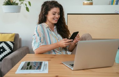 İçişleri Bakanlığı 'nda cep telefonu kullanan mutlu iş kadınları. Gülümseyen iş kadını masasında oturup bilgisayarını ve dijital tabletini hazırlarken telefonuna mesaj yazıyor..
