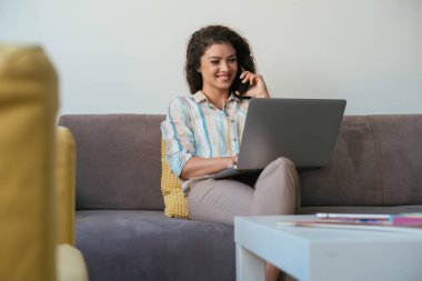 İçişleri Bakanlığı 'nda cep telefonuyla konuşan mutlu iş kadını. Neşeli gülümseyen iş kadını dizüstü bilgisayarı üzerinde çalışırken ve oturma odasındaki kanepede otururken telefonla konuşuyor..