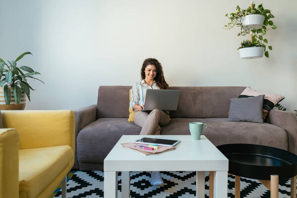 Happy Businesswoman Using a Laptop Computer at Home. Working At Home: Smiling woman typing business report on a laptop keyboard while sitting on a couch in a living room.