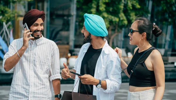 Group Of Smiling Friends Having Fun At The City Street. Three multi-ethnic friends using their mobile phones while talking and laughing together outdoors.