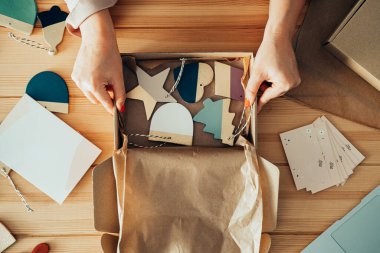 İsimsiz bir kadının dükkanında Clay 'in Noel süslerini paketlediği masa üstü görüntüsü. Küçük Sıfır Atık İş: Atölyesindeki ahşap bir masanın üzerindeki karton bir kutuda teslim edilecek malları paketleyen kadınların el fotoğraflarını kapat.