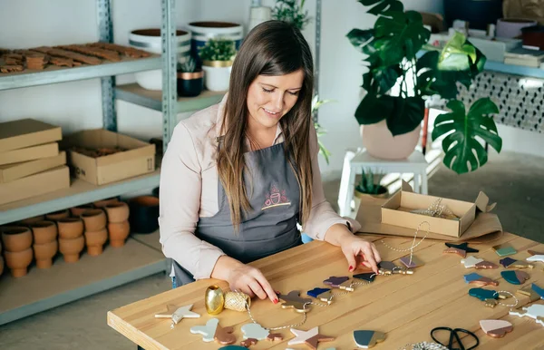 Küçük Çevre dostu İş: Gülümseyen kadın, stüdyosunda masasında otururken el yapımı Noel süsü üretiyor. 