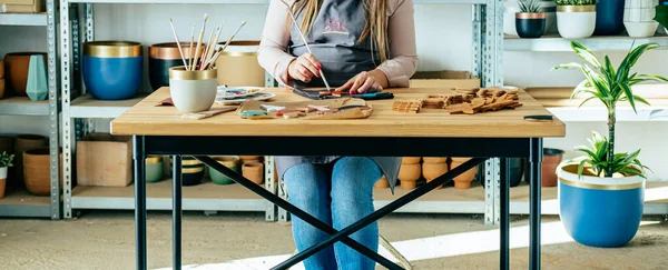 An Anonymous Woman Painting A Star Made Of Clay At Her Studio. Sustainable Business: Unrecognizable woman artisan making handmade ceramics Christmas ornaments while sitting at her workshop desk with her equipment.
