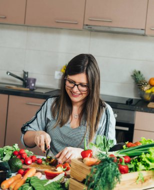 Mutfak masasında organik biber kesen önlüklü gülümseyen kadın.