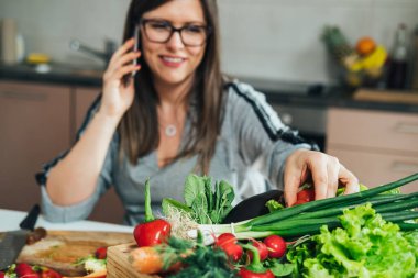 Mutfakta renkli sebzelerle sağlıklı öğle yemeği hazırlarken cep telefonuyla konuşan isimsiz bir kadın.