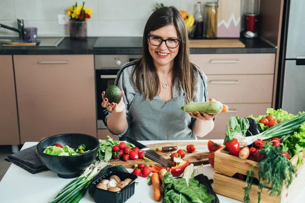 Happy Woman Holding Avocado Zucchini Terwijl Zittend Aan Keuken Bureau — Stockfoto