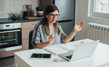Mutfak masasındaki bilgisayardan iş arkadaşlarıyla yapılan bir görüşmede gülümseyen iş kadını konuşuyor.