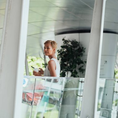 Happy Woman Using Mobile Phone And Drinking Cup Of Coffee While Holding Shopping Bags And Standing At Modern Footbridge