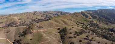 Yüksek bulutlar ve mavi gökyüzü Livermore, California 'nın sakin tepeleri üzerinde bir tepe örtüsü oluşturur. Bu bölge kış aylarında çok ihtiyaç duyulan mevsimsel nem nedeniyle kahverengiden yeşile döner..