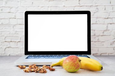 Laptopun önünde sağlıklı yiyecekler. Metin için boş alan. Elma, muz ve fındıkla beyin yemi gibi çalış..                               