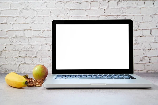 Laptopun sol tarafında sağlıklı yiyecekler var. Metin için boş alan. Elma, muz ve fındıkla beyin yemi gibi çalış..
