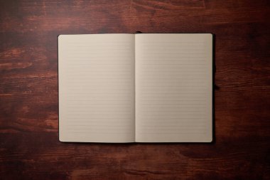 Tahta bir masanın üzerinde duran not defteri. Masa lambasından akşam havası. Fikirler, notlar ve günlük için defteri aç. Bilgi için uzayı kopyala. Üst görünüm.  
