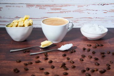 Bulletproof coffee in a white cup. Coconut oil, butter and coffee beans can be seen. Spoons in front of the cup. Close up. Bulletproof coffee is part of the ketogenic diet. Low carb diet.                  