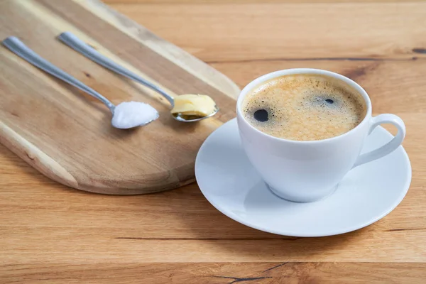 Bulletproof coffee with two spoons on a wooden table. Coconut oil and butter on the spoons. The keto coffee is part of the keto diet. A low carb diet. Ketogenic recipe.