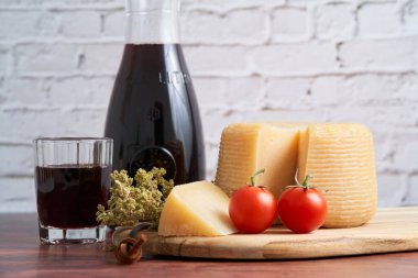 Italian hard cheese such as pecorino or caprino, wine with carafe and traditional glass, tomato and oregano. Sliced dried cheese with a bunch of oregano on a wooden board.                           clipart