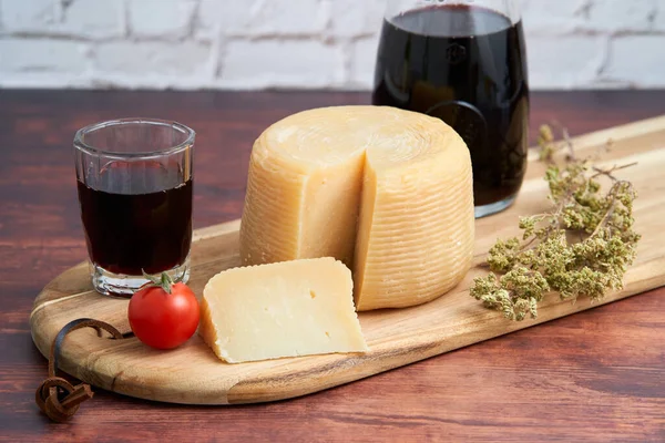 Pecorino ya da caprino gibi İtalyan sert peyniri, Carafe 'de şarap ve tahta bir tahtanın üzerinde dilimlenmiş peynirli keklik otu. Geleneksel İtalyan şarap kadehi ve domates.                            