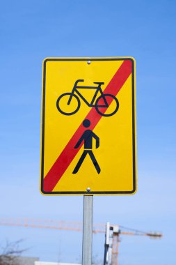 Sign with the information that the diversion for pedestrians and cyclists has ended. Black symbols and red crossed out stripe on yellow traffic sign.