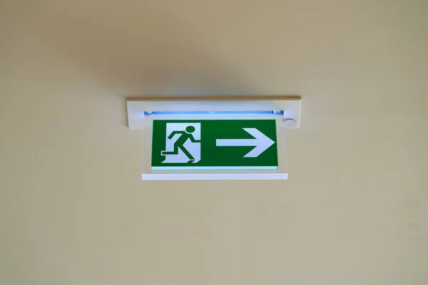 An emergency exit sign with an arrow pointing to the right hangs under a ceiling.