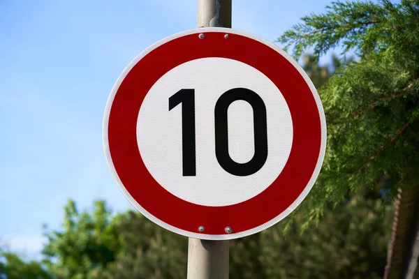 Trafik levhası hız limitinin saatte 10 km ya da 10 mil olduğunu gösteriyor. Mavi gökyüzü ve arka planda odak dışı ağaçlar.                               