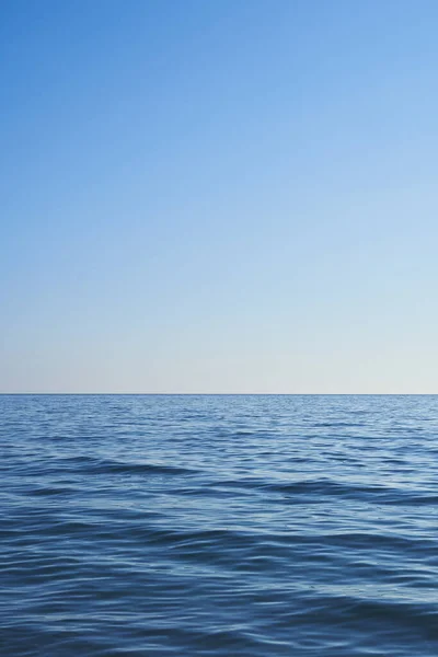 Dark blue water from the sea with blue sky. Light comes from the right. Vertical format, also suitable as a poster or background. Free space for text or objects.                            