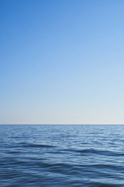 Dark blue water from the sea with blue sky. Light comes from the right. Vertical format, also suitable as a poster or background. Free space for text or objects.                               
