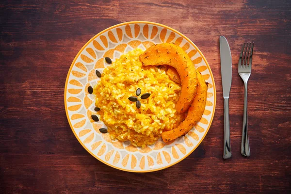Kabak dilimli balkabaklı risotto tahta bir masanın üzerinde yukarıdan fotoğraflandı. Dekorasyon olarak kabak tohumları. Bıçak ve çatal tabağın yanında. İtalyan tarifi.                               