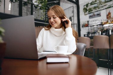 Kafede otururken dizüstü bilgisayarda çalışan güzel bir kadın.
