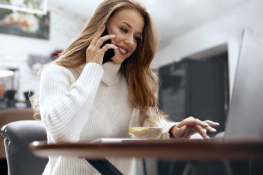 Telefonla konuşurken dizüstü bilgisayarda çalışan bir kadın. Çevrimiçi Görev