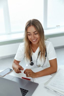 Bayan doktor bilgisayarında video görüşmesi yapan bir hasta var. Genç kadın terapist asistanı web kamerasına video konferans yapıyor..  