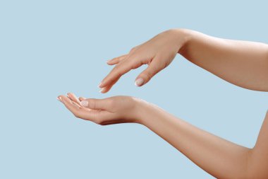 Tırnakları Fransız manikürlü güzel kadın ellerine yakın çekim. Mavi arka planda izole edilmiş, krem sürme, masaj. El bakımı.