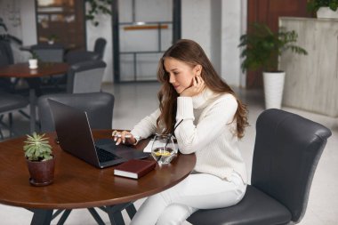 Kafede otururken dizüstü bilgisayarda çalışan genç bir kadın.