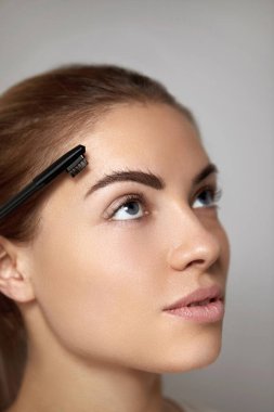 Kaş makyajı. Kaşlarını tarakla şekillendiren güzel bir kadın. Profesyonel makyajlı kaş hatları olan güzel kız modeli.
