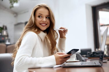 Günlük giysiler içinde, çalışırken dizüstü bilgisayar kullanan ve gülümseyen güzel bir genç kadın.