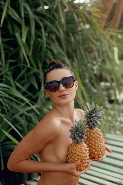 Tropikal arka planda poz veren genç ve güzel bir kız, elinde ananaslarla. Bikinili bronz tenli kadın.. 