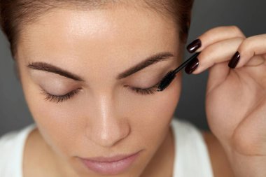 Mascara. Makyaj fırçasıyla kirpiklerine siyah rimel süren bir kadın. Güzel, genç bir kadın yüzü, doğal kaşları ve kirpikleriyle..  