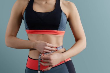 Kilo kaybı, zayıf vücut, sağlıklı yaşam tarzı konsepti. Formda fitness kızı ölçü bandıyla belini ölçüyor.