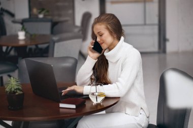 Dizüstü bilgisayarda çalışan, cep telefonuyla konuşan bir kadın..