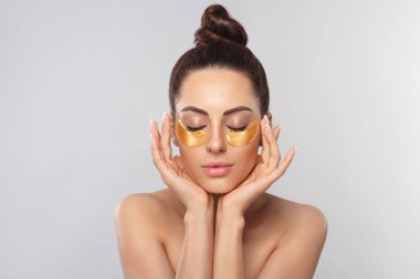 Sağlıklı, mükemmel cilde sahip güzel bir kadın yamaları tutuyor. Altın kozmetik kolajen hidrojel bantlı güzel yüz. Kırışıklık önleyici maskeyi gözlerimin altında kaldırıyorum. Cilt bakımı kavramı
