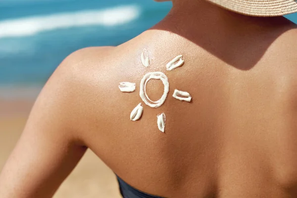 Woman Applying Sun Cream on Tanned Shoulder In Form Of The Sun. Sun Protection.Sun Cream. Skin and Body Care. Girl Using Sunscreen to Skin. Female Holding Suntan Lotion and Moisturizing Sunblock.