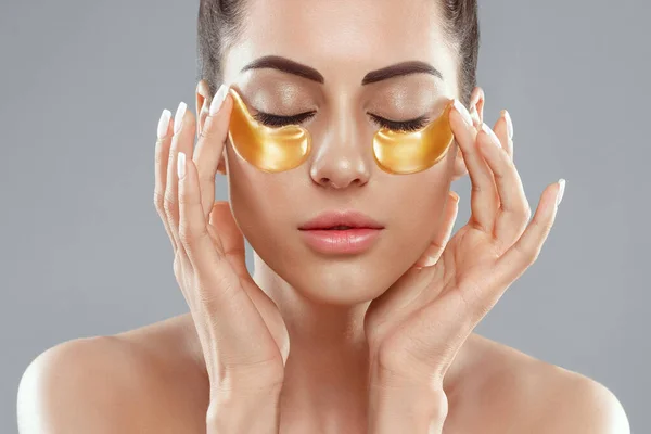 Beautiful woman with healthy perfect skin holds patchs. Beauty face with gold cosmetics collagen hydrogel patch. Lifting anti-wrinkle mask under eyes. Skincare concept.