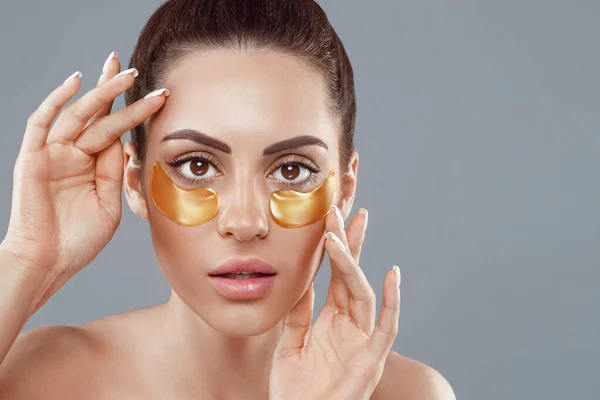 Beauty woman face with under eye collagen gold pads.  Anti-aging moisturizing eye mask, golden hydrogel patches, eye skin treatment, cosmetology.