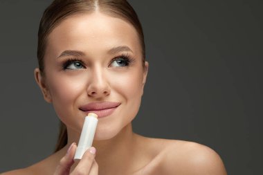 Lips Skin Care. Beautiful Woman Face With Lips Applying Hygienic Lip Balm, Lip Care Stick. Closeup Of Female Face With Soft Skin Putting Lip Protector Lipstick On. Beauty Cosmetics Concept. clipart