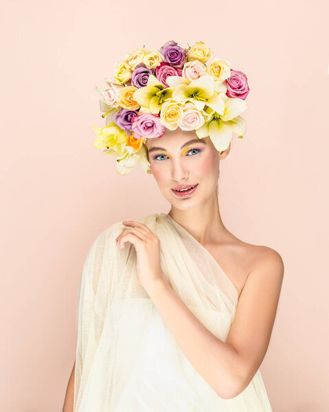 Young beautiful woman with bouquet of flower in head. Art portrait of sexy blonde with colorful flowers. Professional art makeup. Pretty pink background. Happy concept